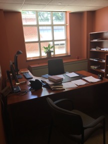 Office with desk, chair, computer, telephone, bookshelves and paperwork.